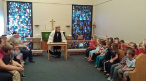 Person in robe speaking to children in a room