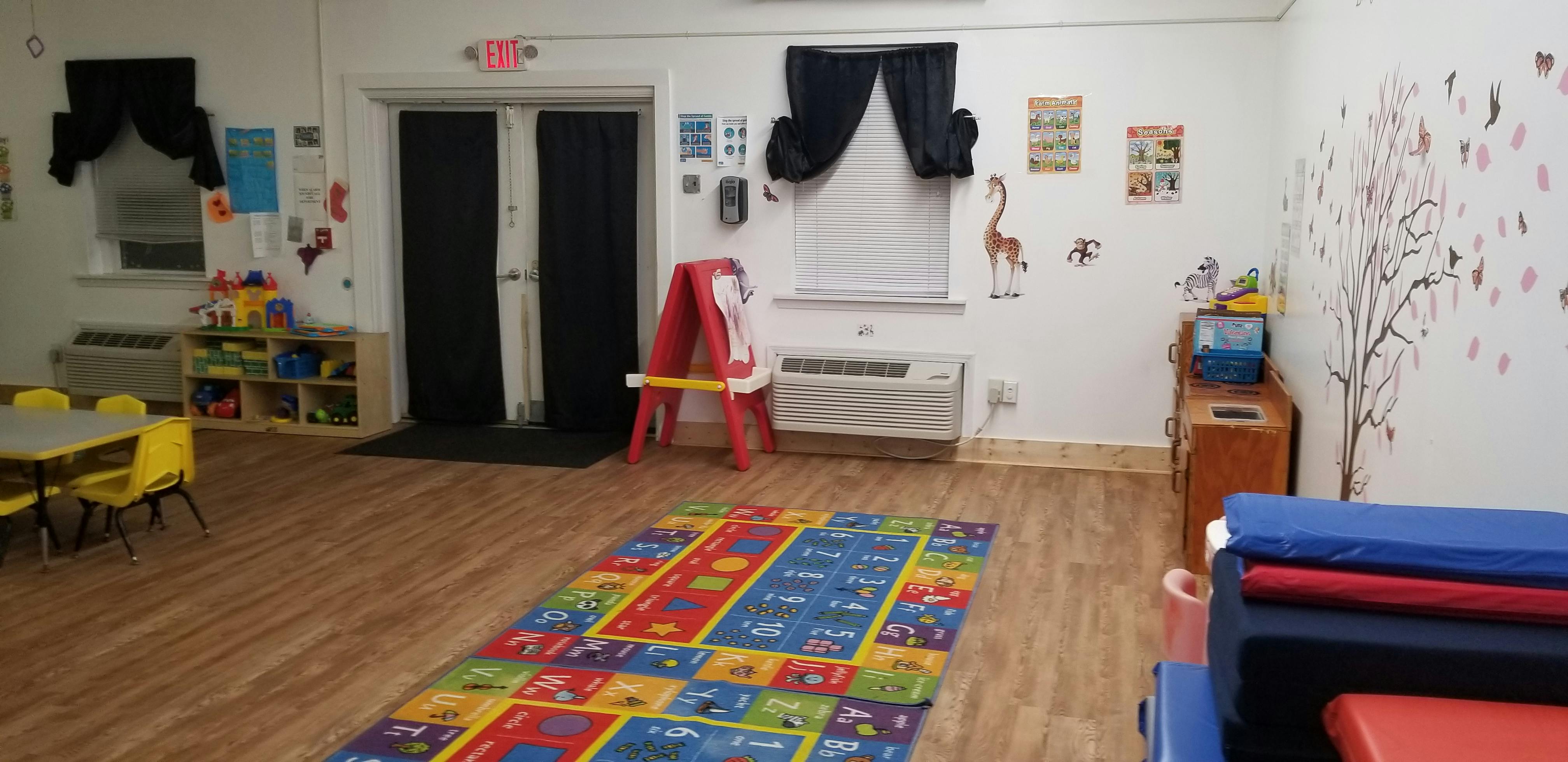 Empty classroom with colorful rug, small tables, and an easel