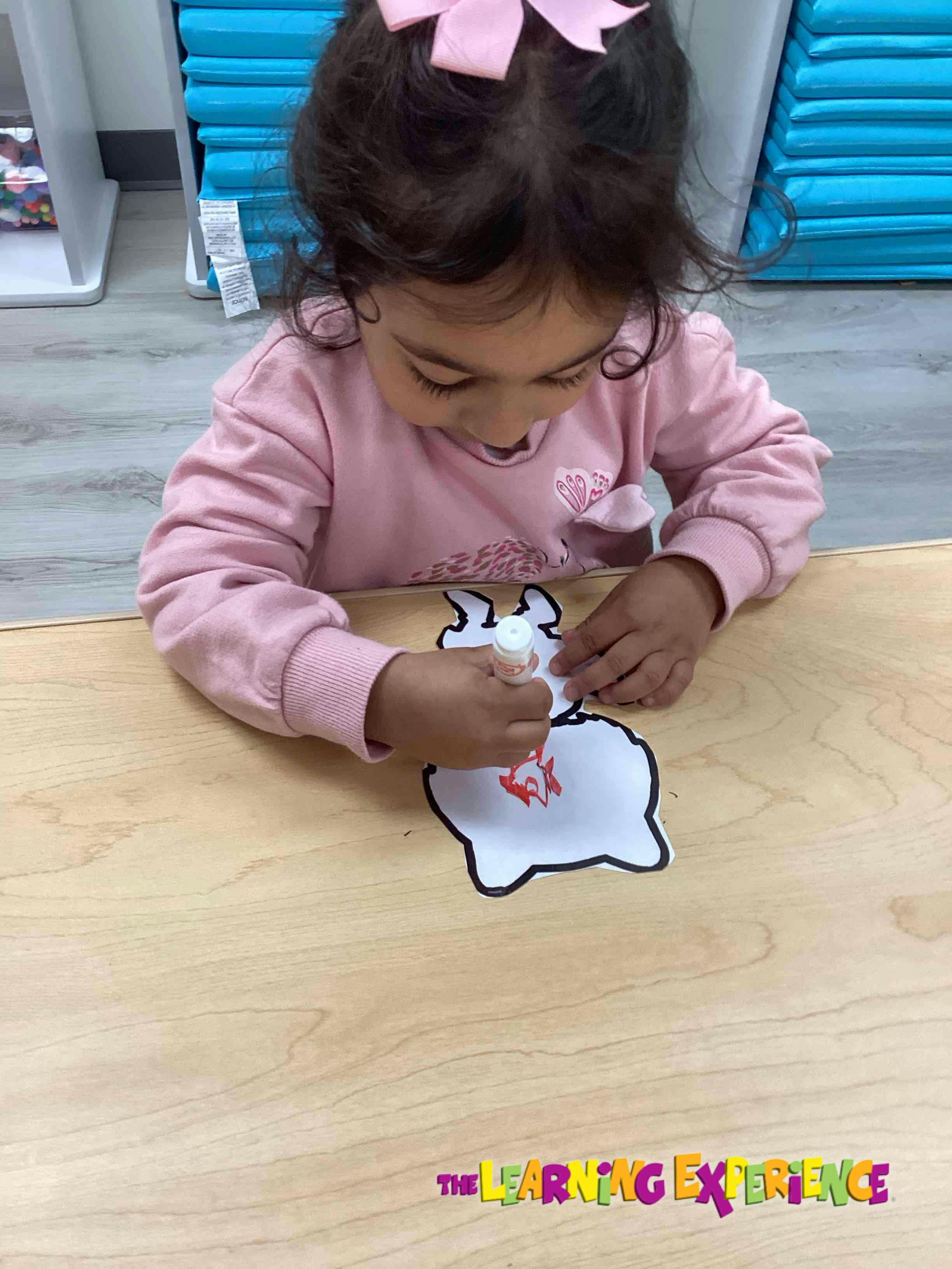 Child decorating a paper cutout on a wooden table