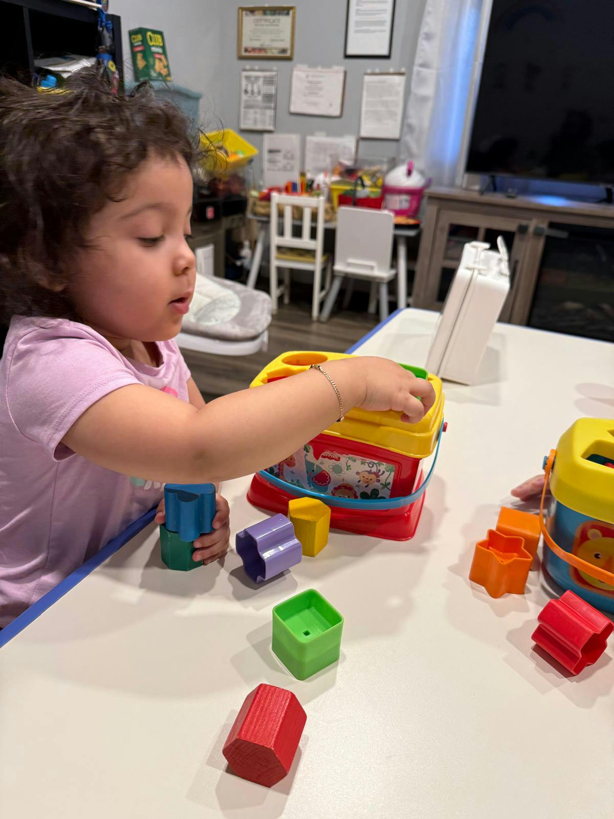 Child playing with a shape sorter toy and colorful blocks on a table
