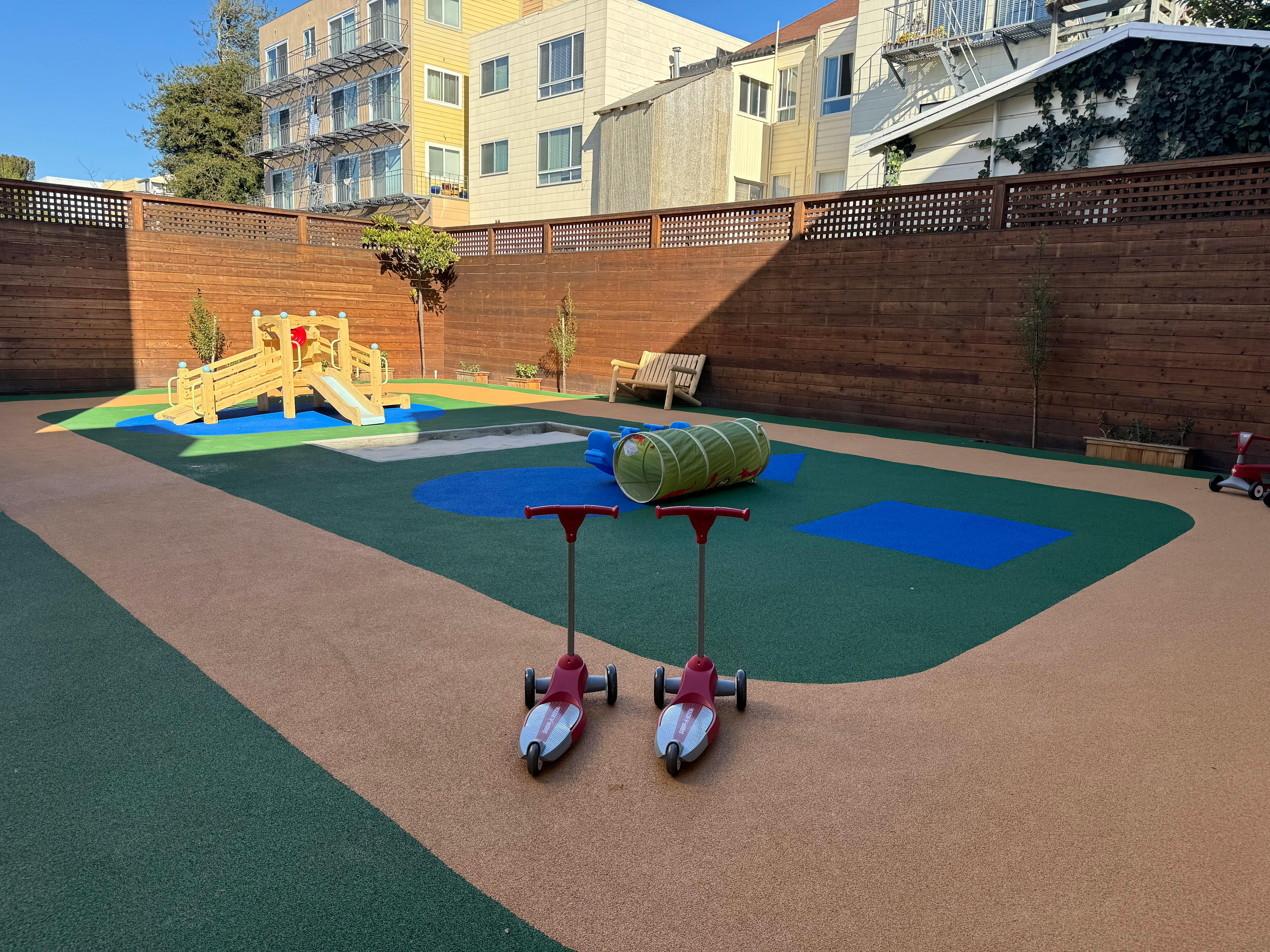 Two scooters on a playground with a wooden play structure and tunnel