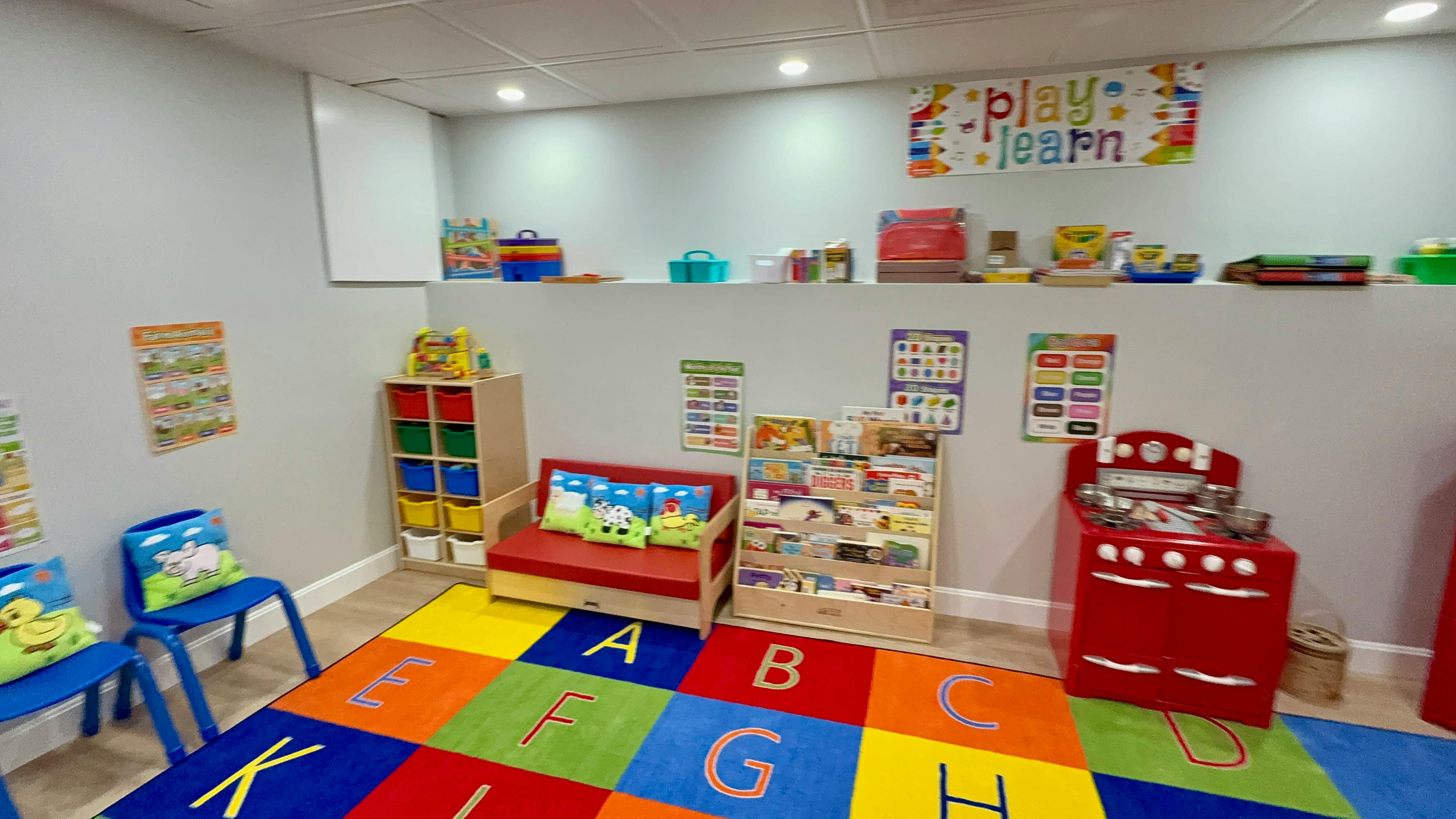 Playroom with colorful alphabet rug, small chairs, and toy kitchen