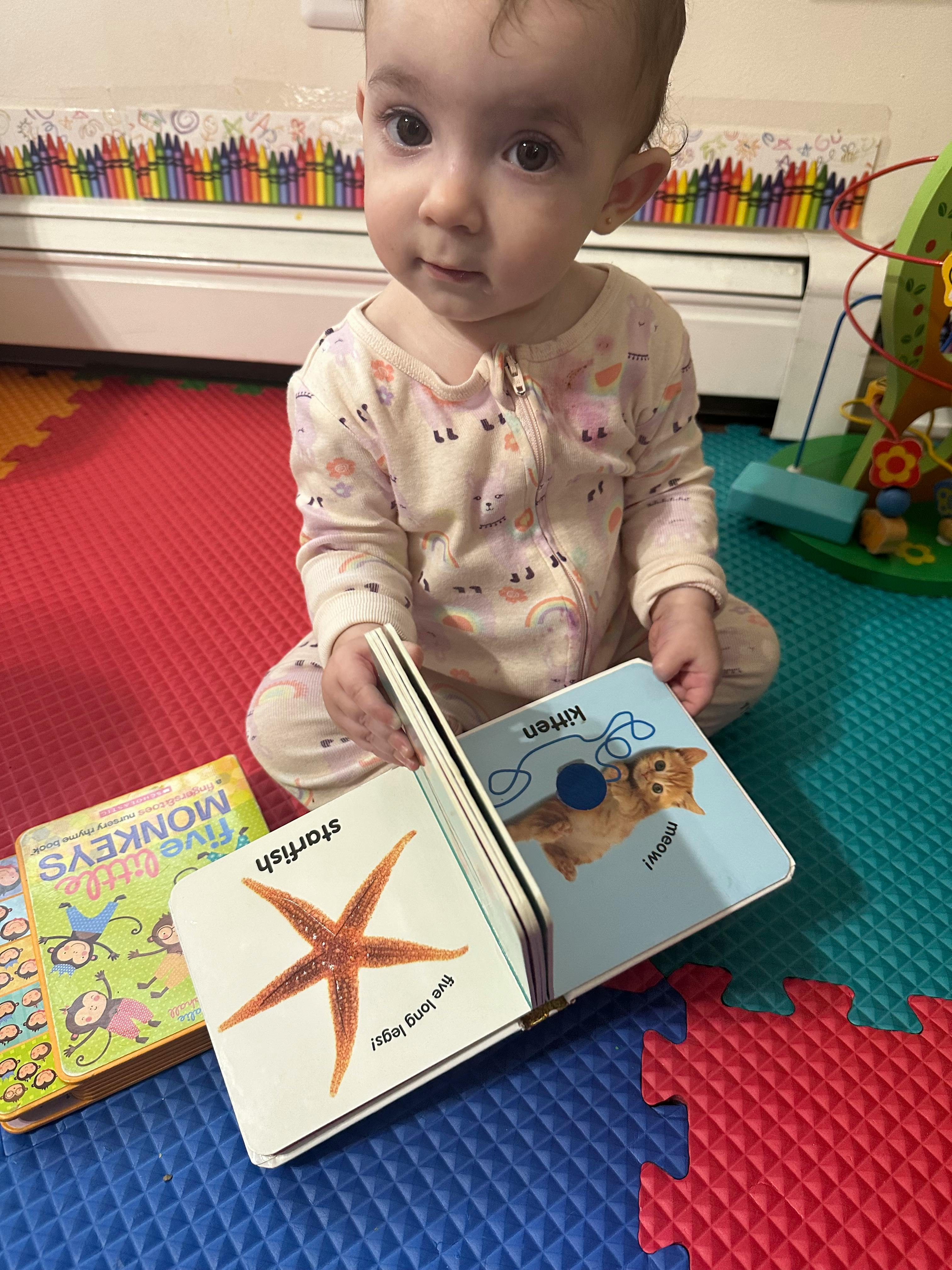 Child sitting on floor holding an open board book