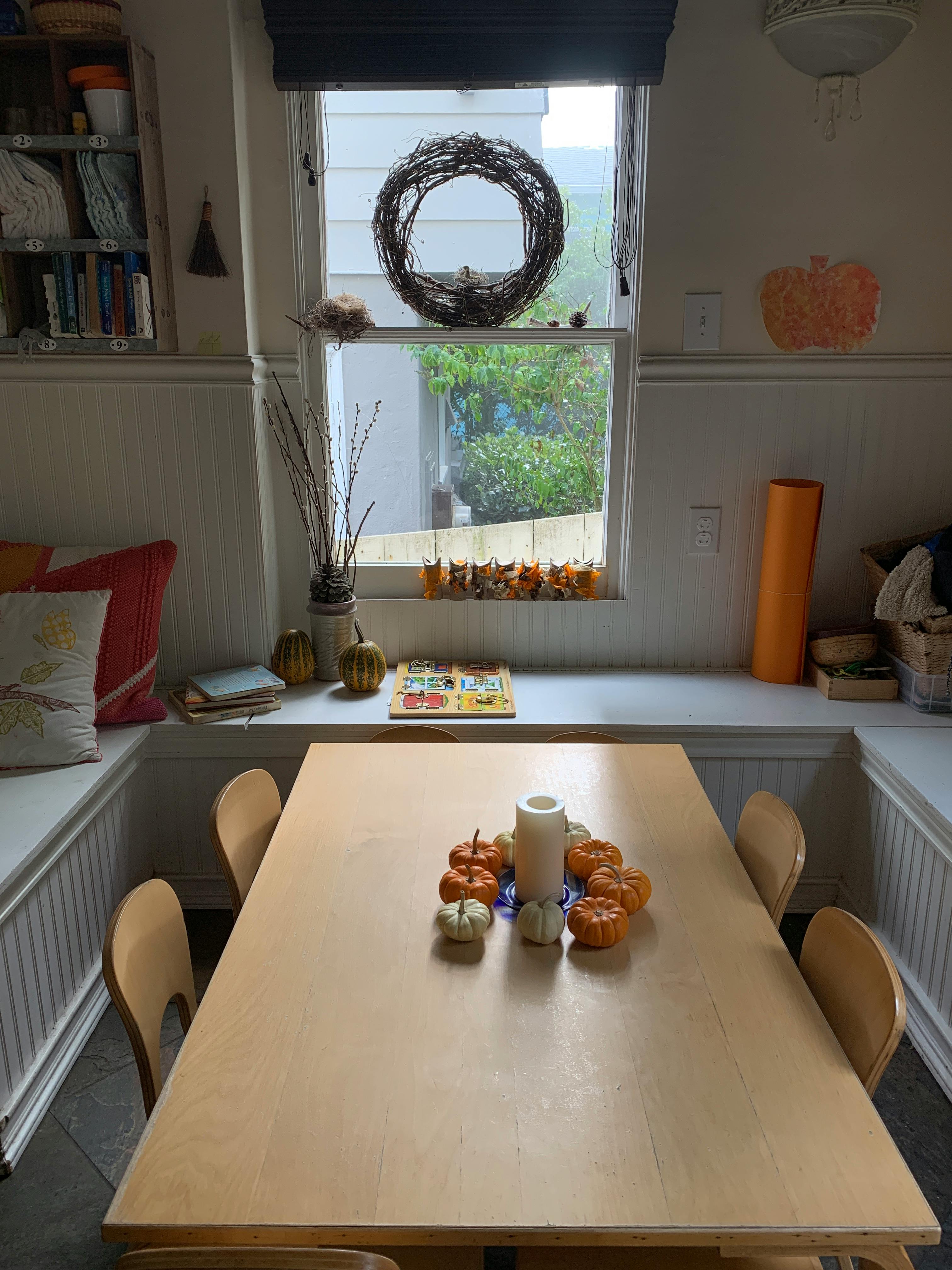 Dining table with chairs and a centerpiece of small pumpkins and a candle