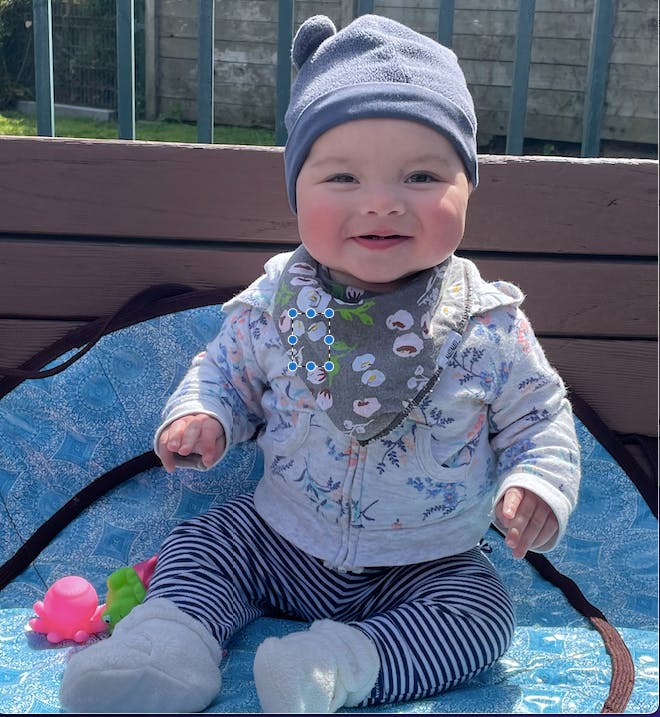 Child in a hat and bib sitting on a blanket outdoors