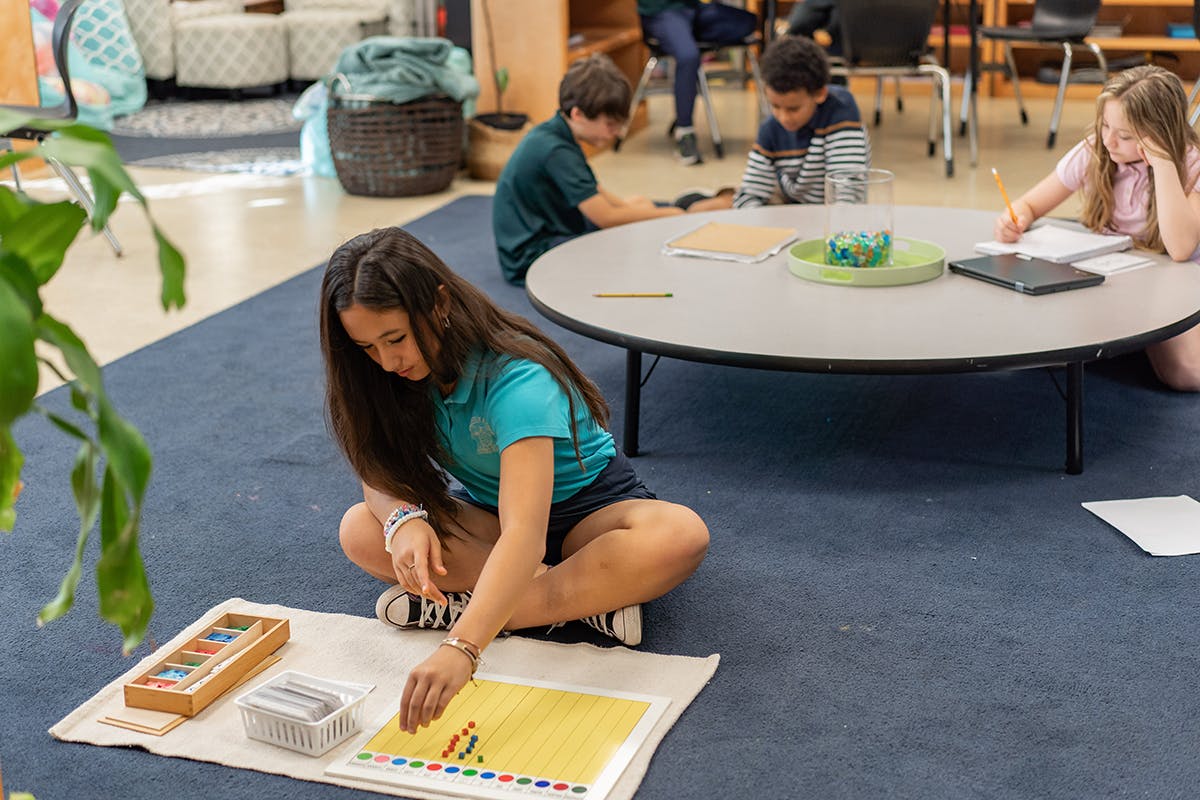 Child on floor working with colorful blocks, other children at a table