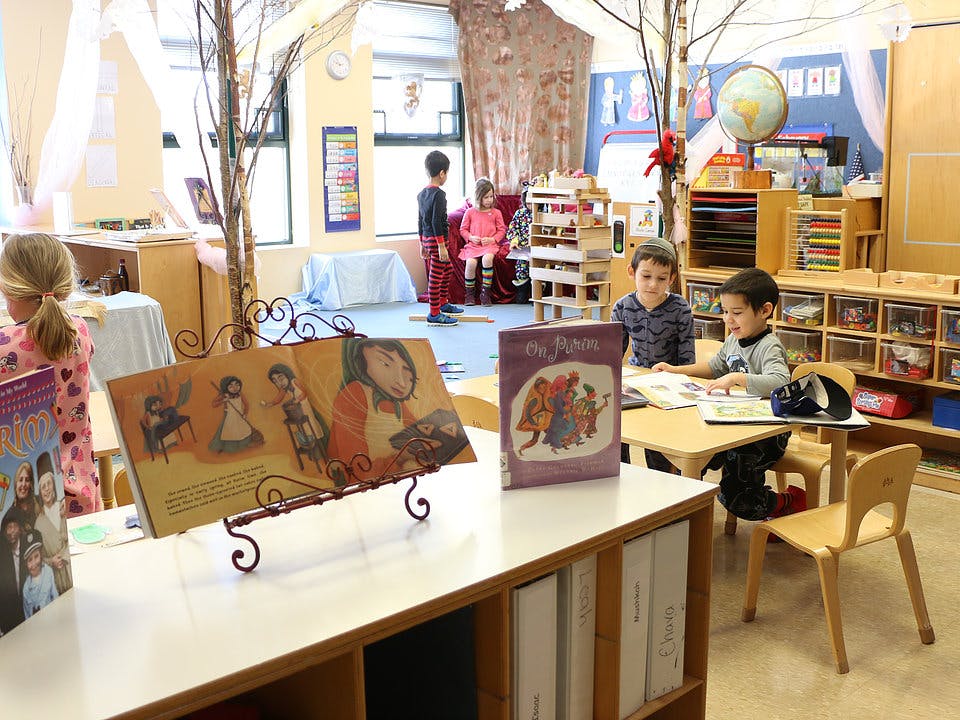 Children in a classroom, some at desks, others standing