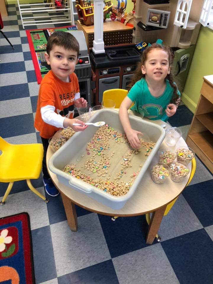Two children playing with cereal and sprinkles in a sensory bin