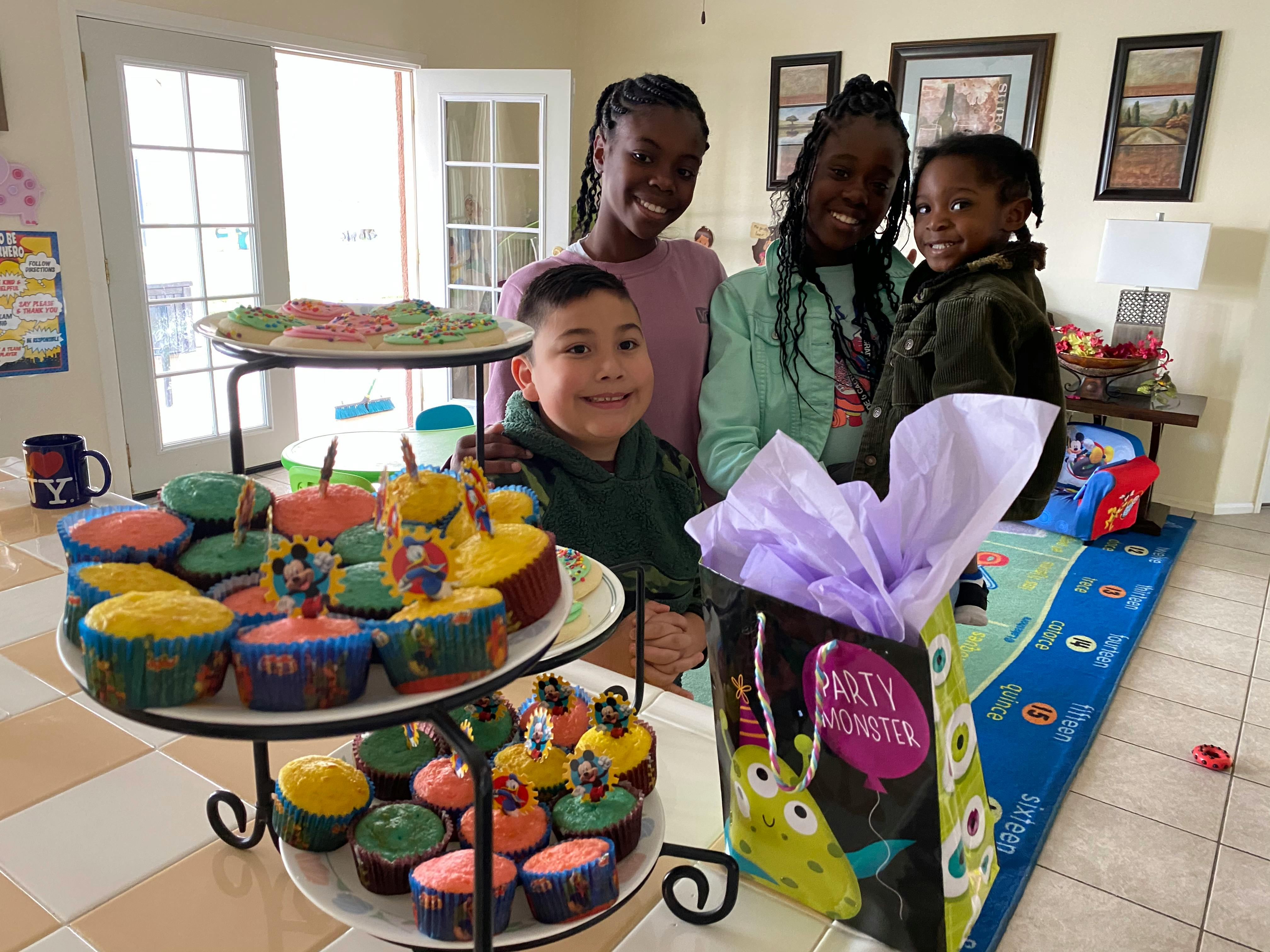 Three children and one teen smiling with cupcakes and a gift bag