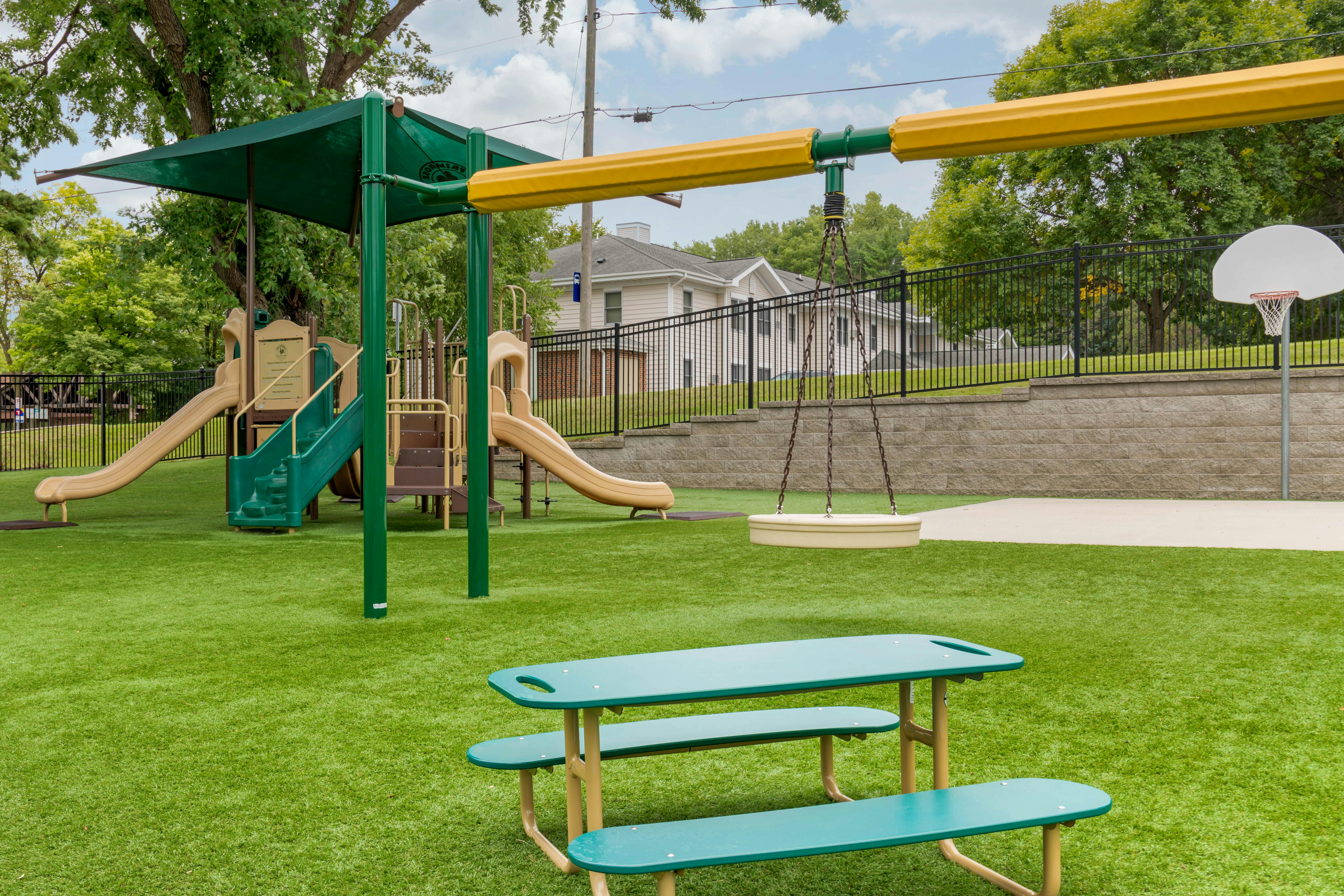Playground with swings, slides, a basketball hoop, and a green picnic table