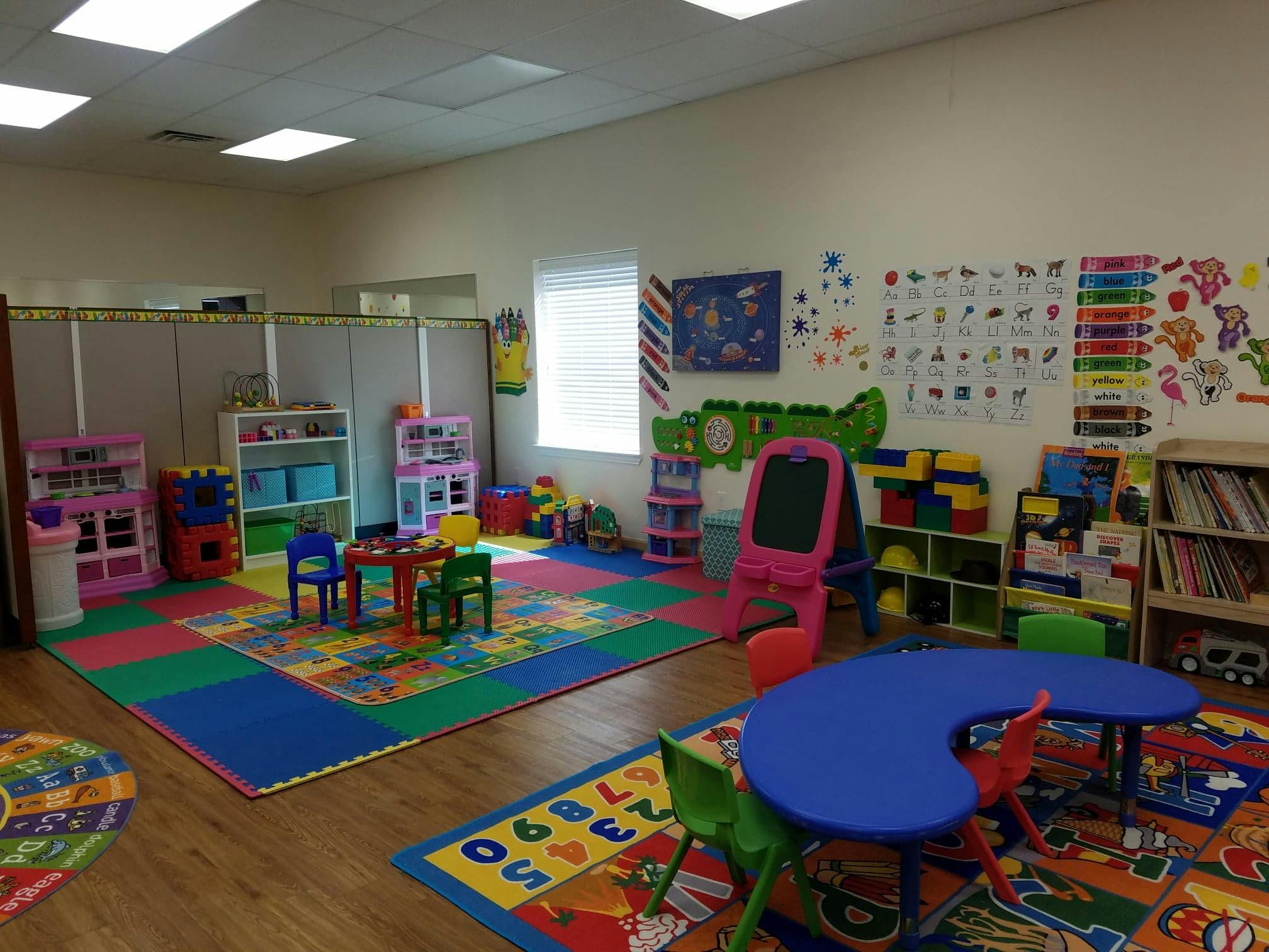 Playroom with colorful mats, small tables, chairs, and toys
