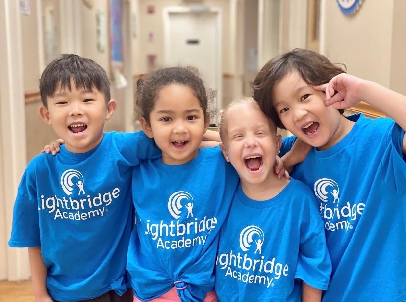 Four children in blue Lightbridge Academy shirts smiling