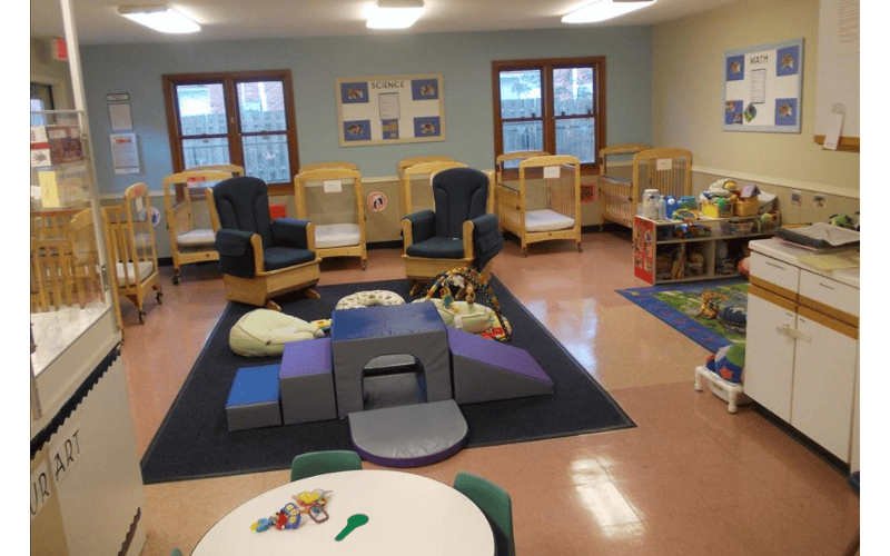 A playroom with cribs, rocking chairs, play mats, and a small table with chairs