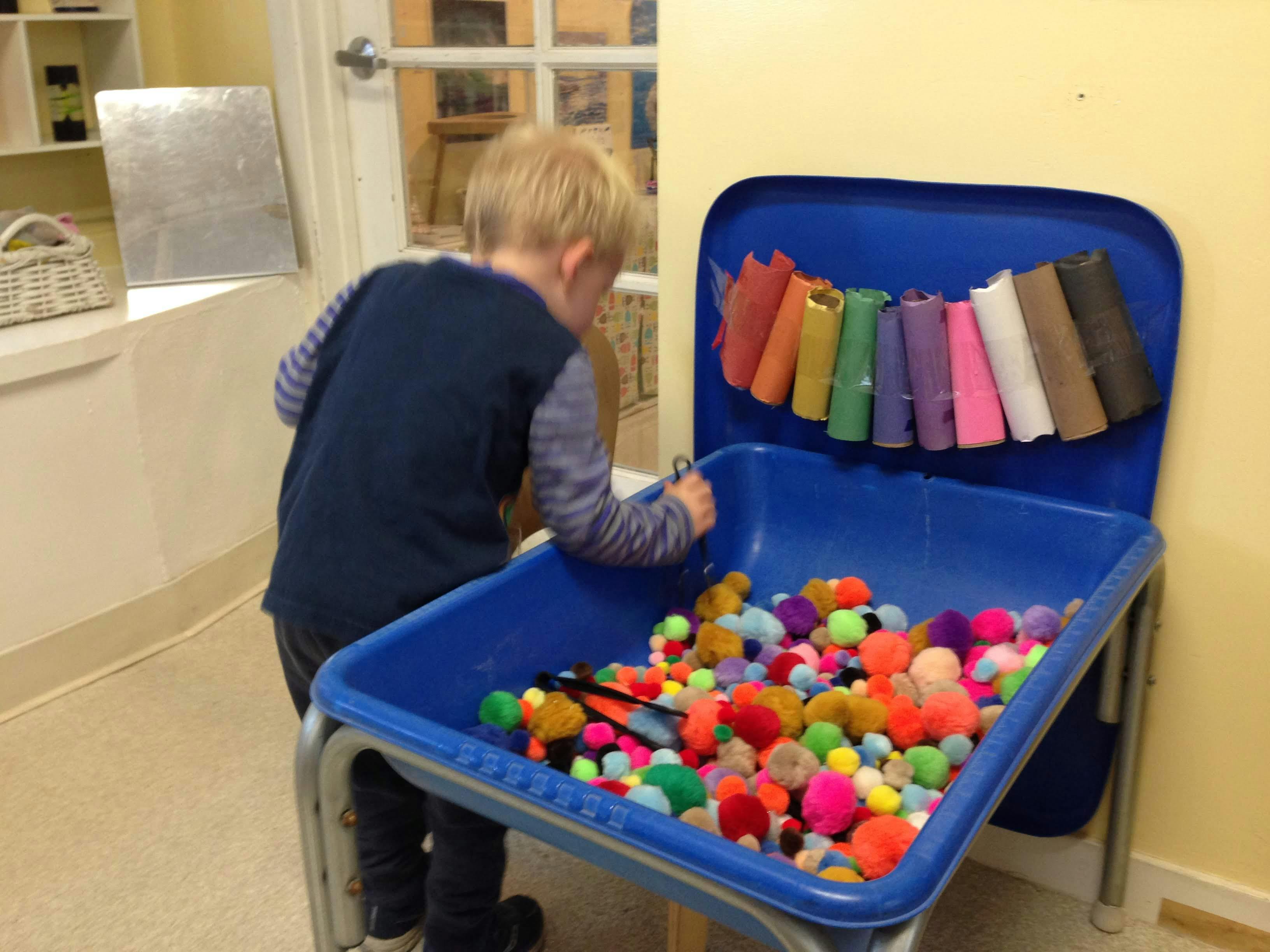 Child playing with colorful pom-poms in a blue bin