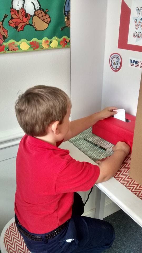 Child placing a paper into a red box at a voting booth
