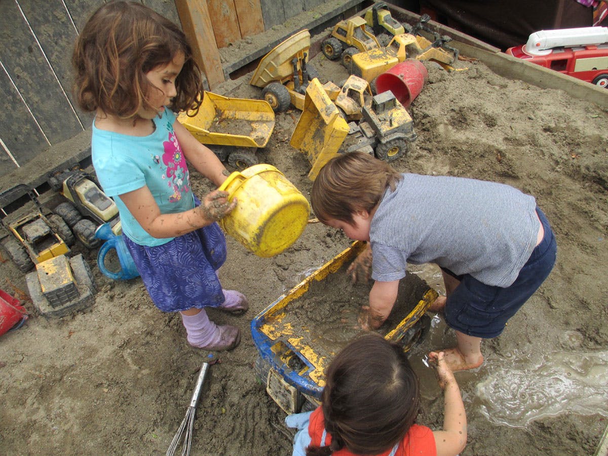Children playing in a sandbox with toy trucks and buckets
