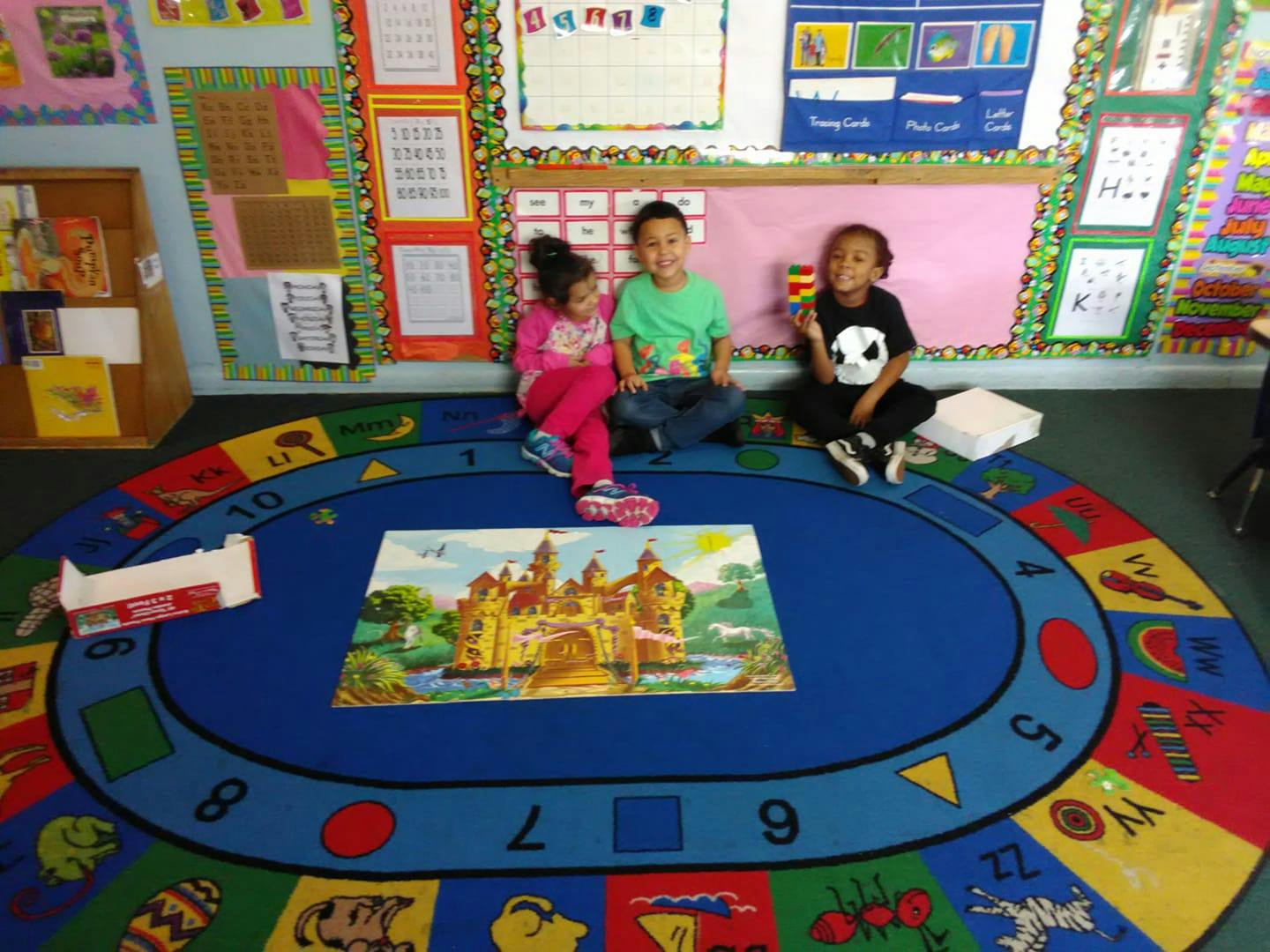 Three children sitting on a colorful rug with a puzzle in front of them
