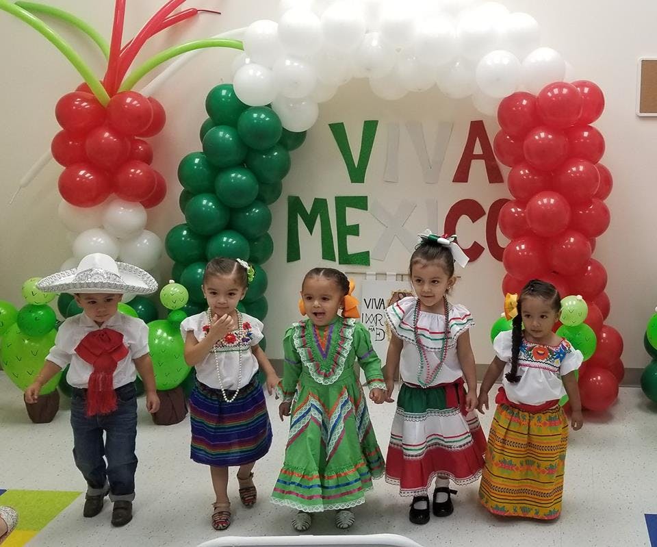 Children in traditional clothing standing in front of a balloon arch