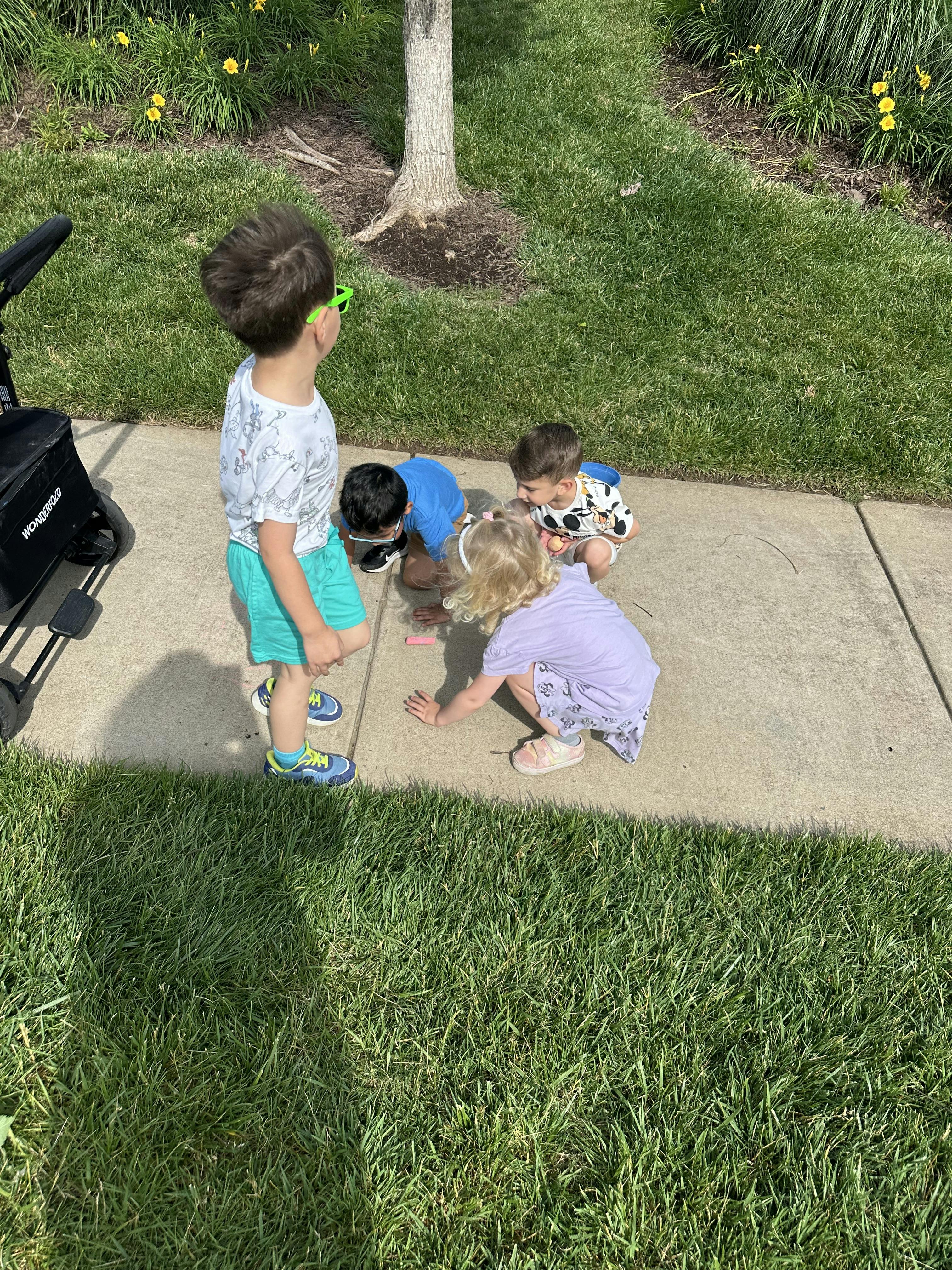 Four children playing with chalk on a sidewalk