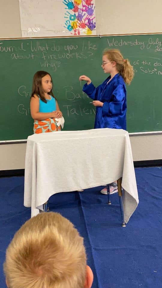 Two children standing in front of a chalkboard with writing