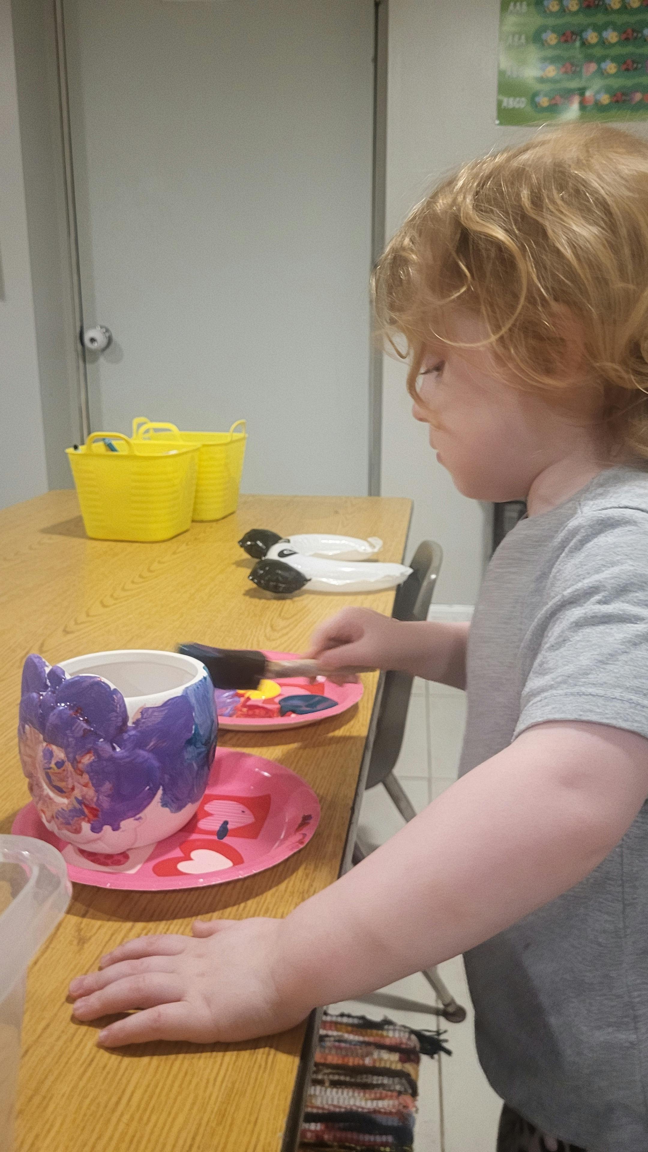 Child painting a ceramic mug at a table
