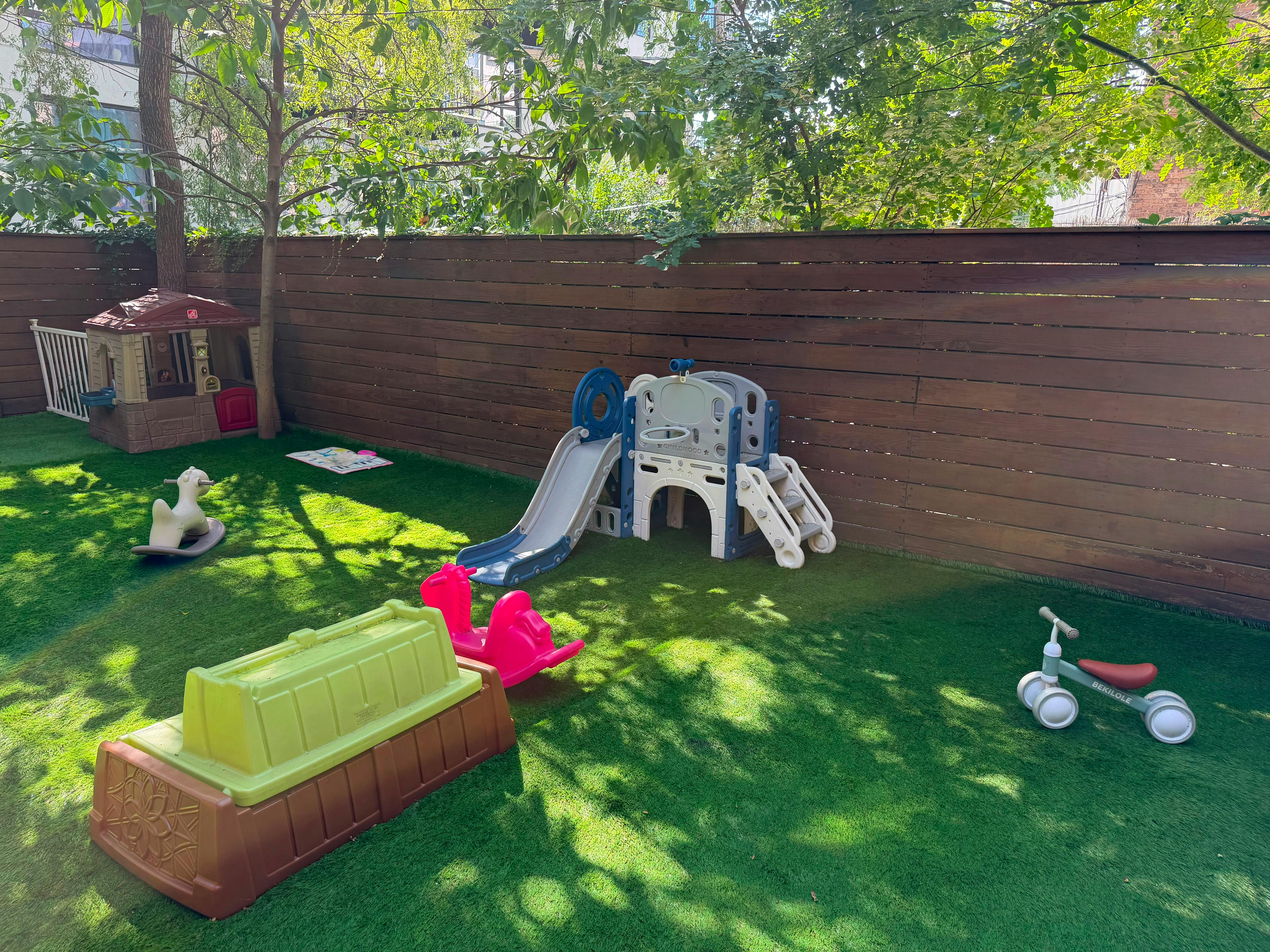 Plastic playground equipment and toys on a grassy lawn with a wood fence