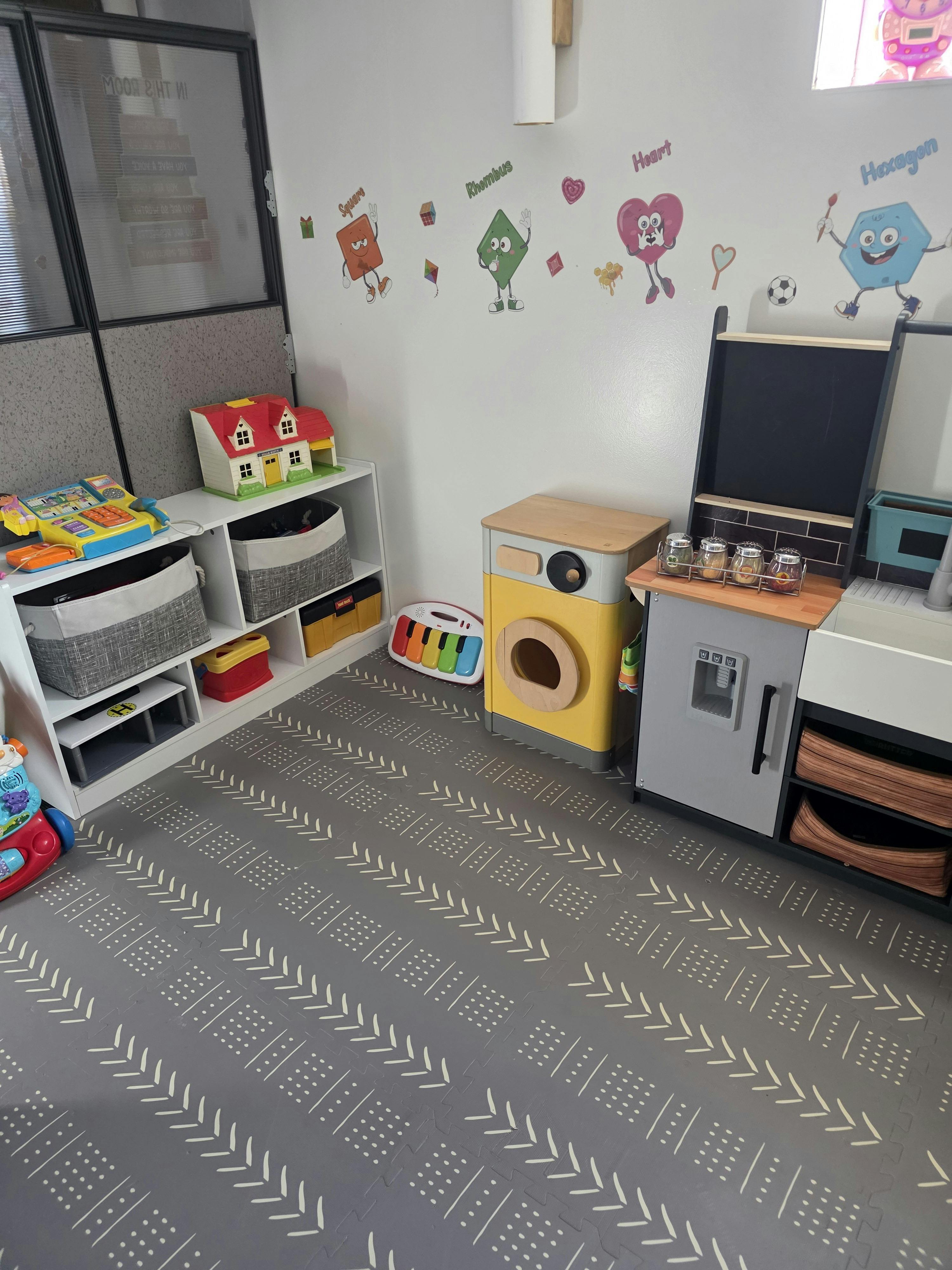 Play area with toy kitchen, washer, and shelves containing children's toys