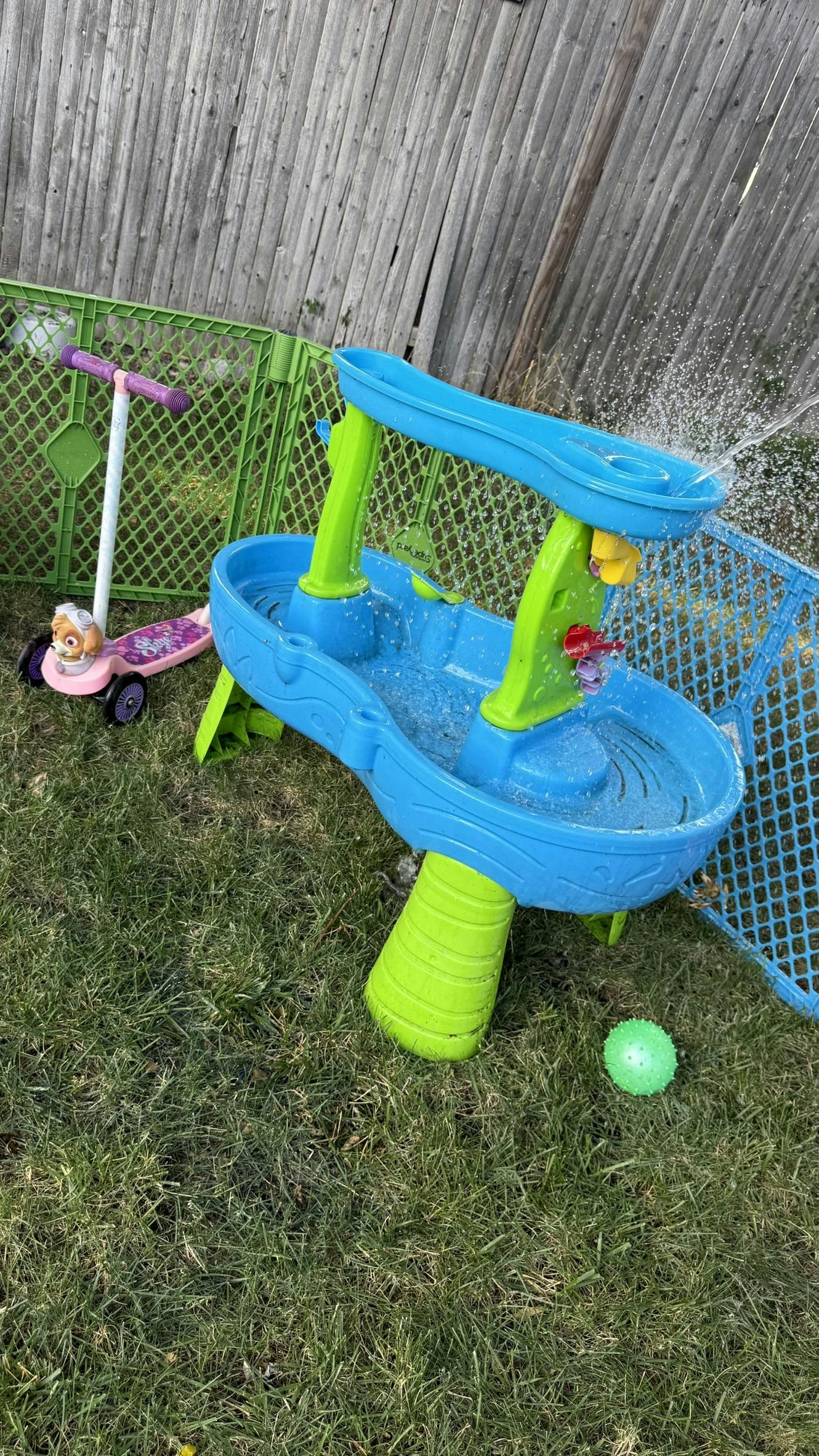 Water table with water spraying, scooter, and green ball on grass