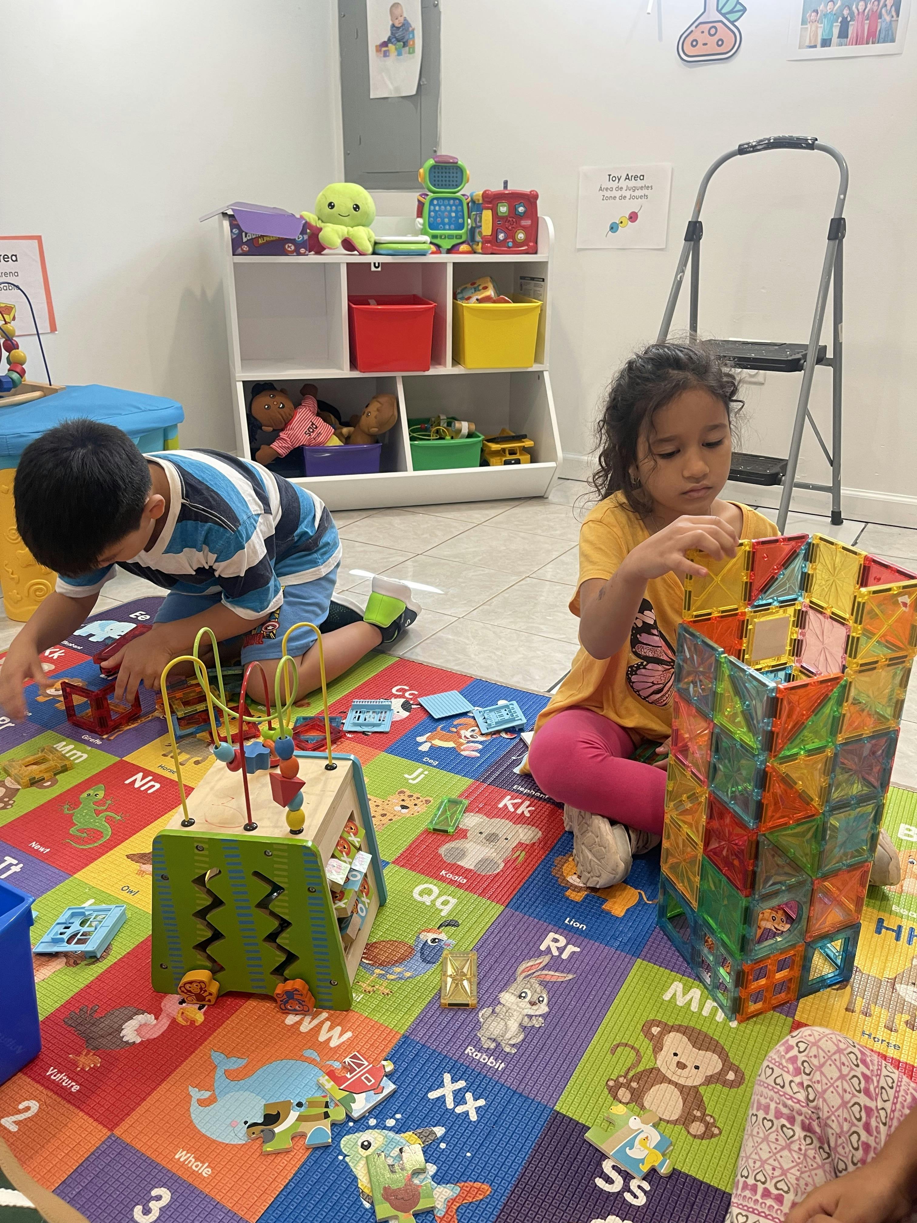 Two children playing with colorful magnetic tiles and a bead maze on a floor mat