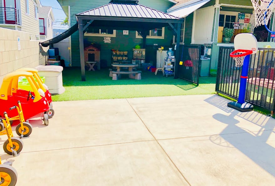 Outdoor play area with a red toy car, tricycle, and basketball hoop