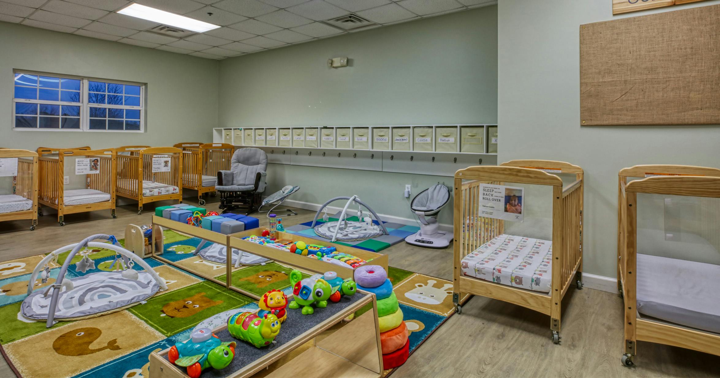 A room with several cribs, a rocking chair, play mats, and baby toys