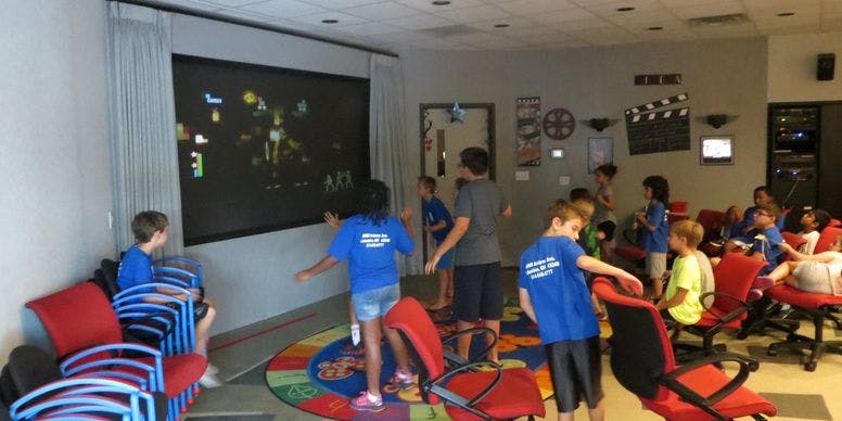 Children watching a large screen in a room with chairs