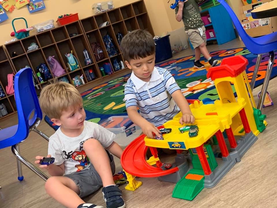 Two children playing with a toy car garage in a classroom