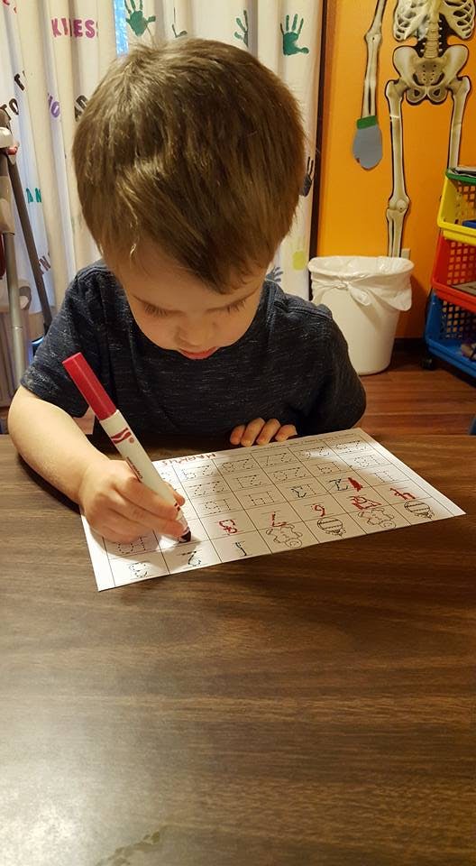 Child writing on a paper with a red marker