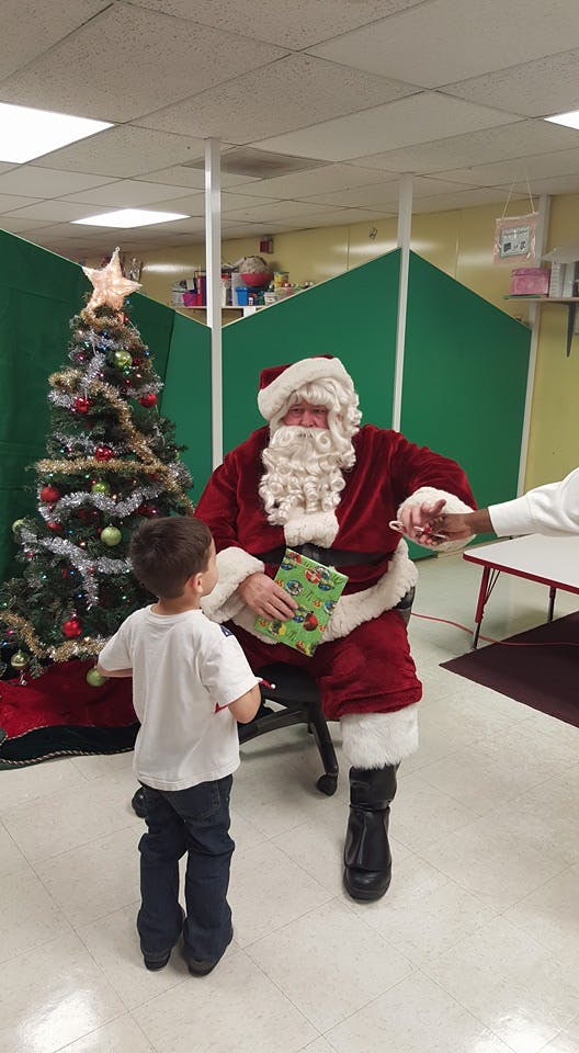 Santa Claus giving a gift to a child next to a Christmas tree