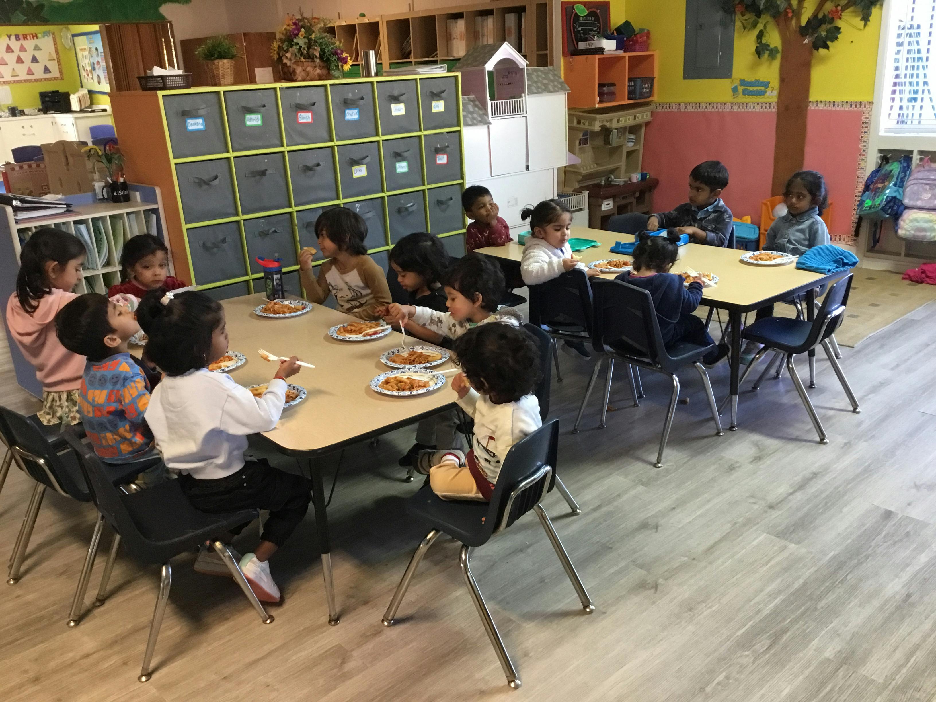 Children sitting at tables and eating meals in a classroom
