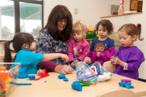 Adult and four children playing with modeling clay at a table