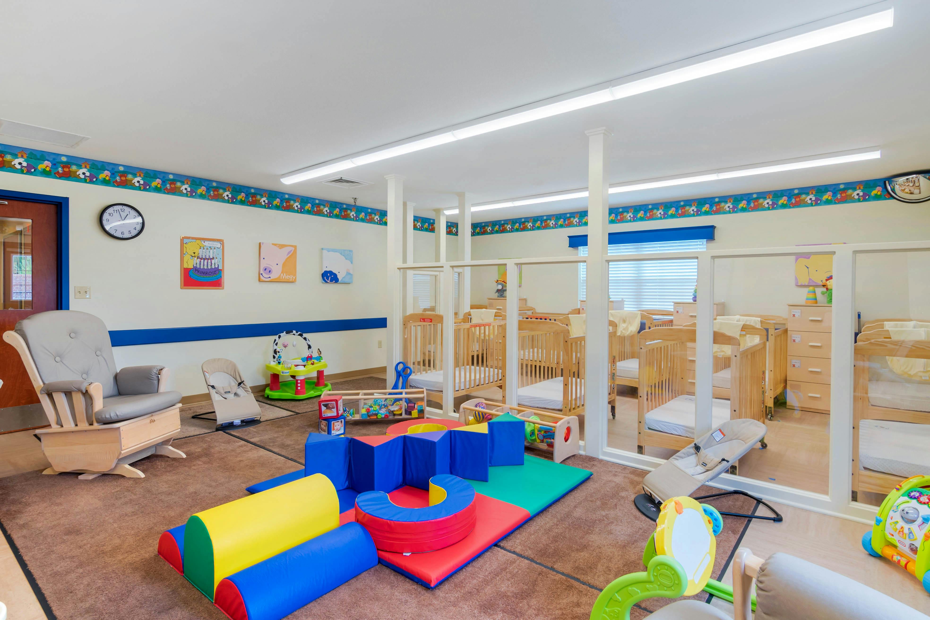 A colorful childcare classroom with several cribs and soft play equipment