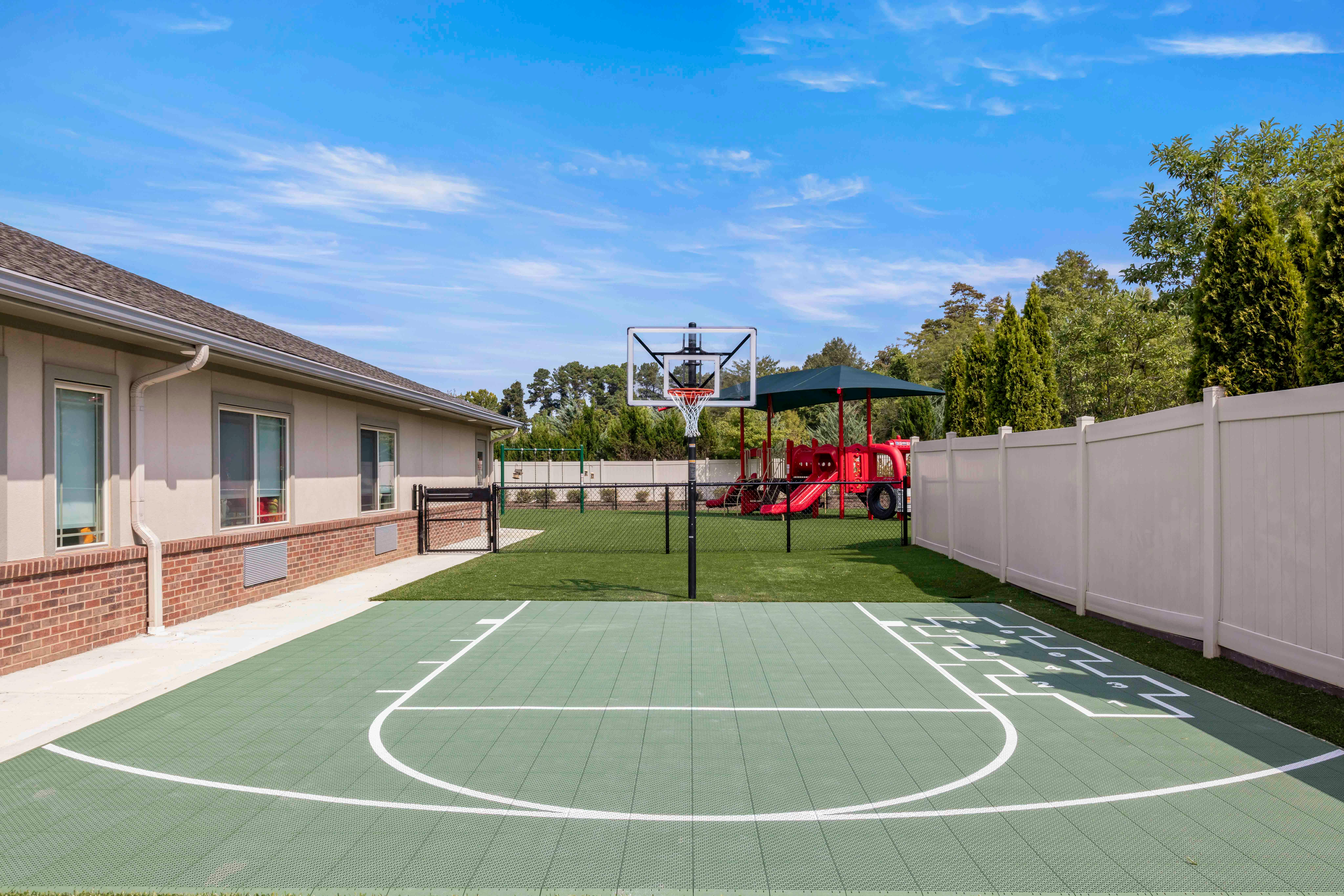 Outdoor playground with basketball hoop, red slide structure, and hopscotch