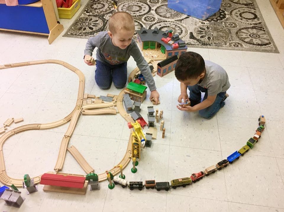 Two children playing with a wooden train set on the floor