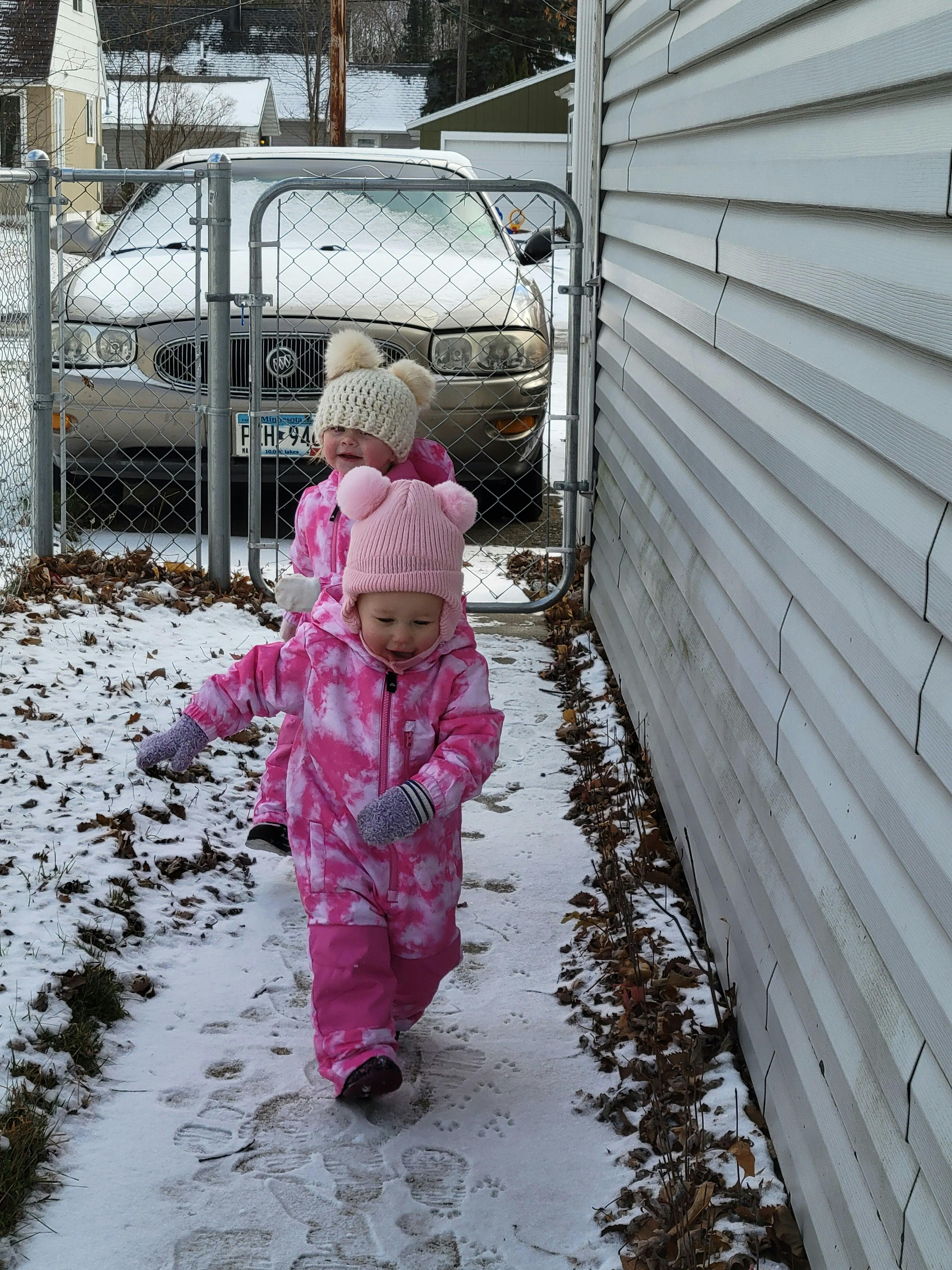 Two children in winter clothing standing next to a fence in the snow