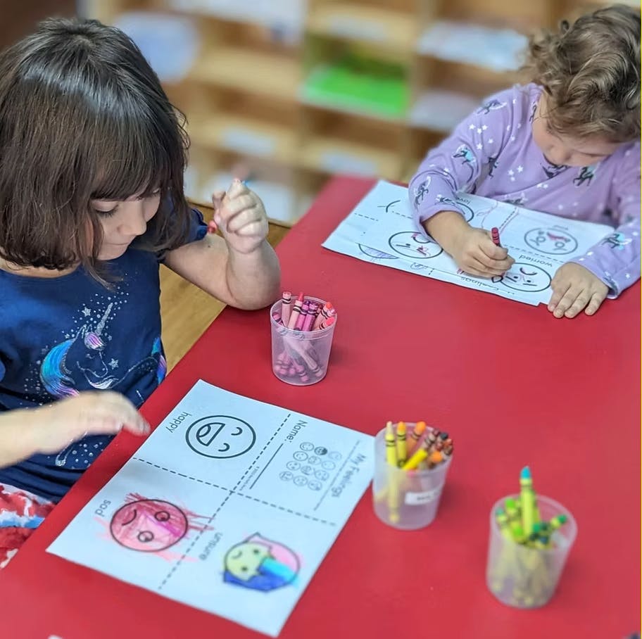 Two children coloring feelings charts with crayons