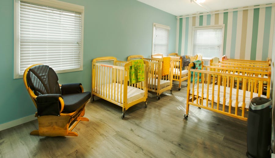 Room with multiple cribs and a rocking chair