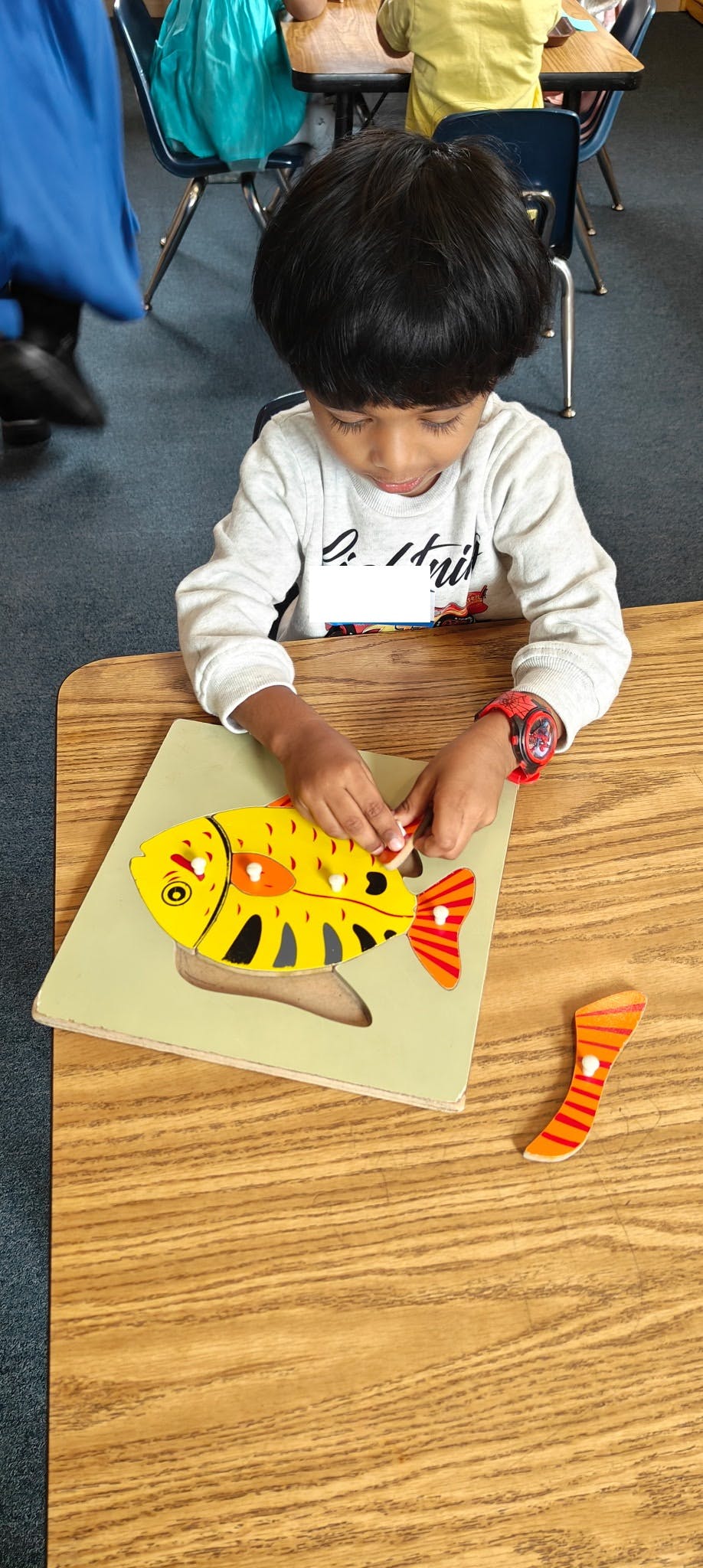 Child playing with a fish-shaped puzzle on a wooden desk