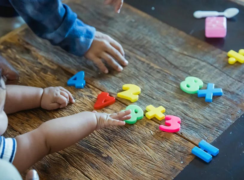 People playing with plastic number and math symbols on a wooden table