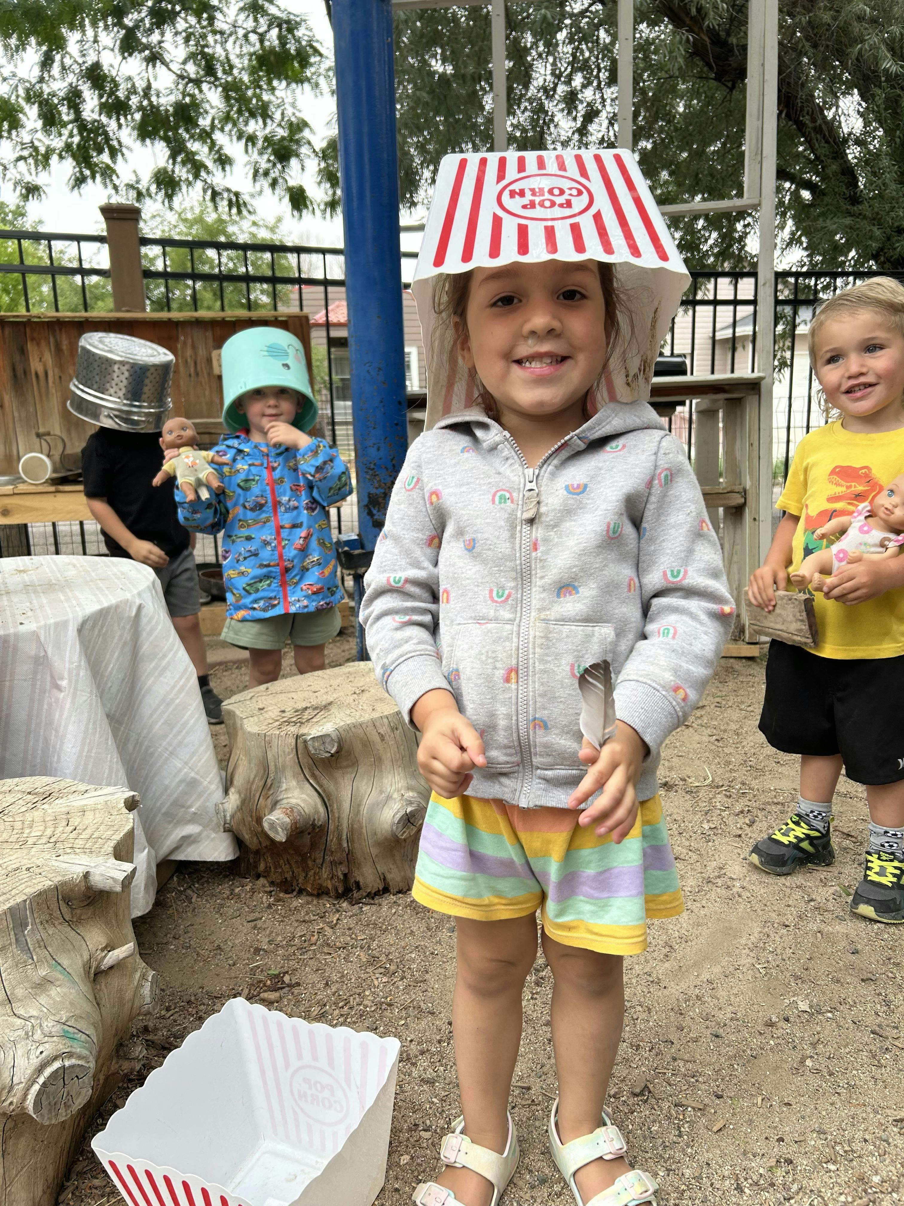 Child wearing a popcorn box on their head, standing with other children