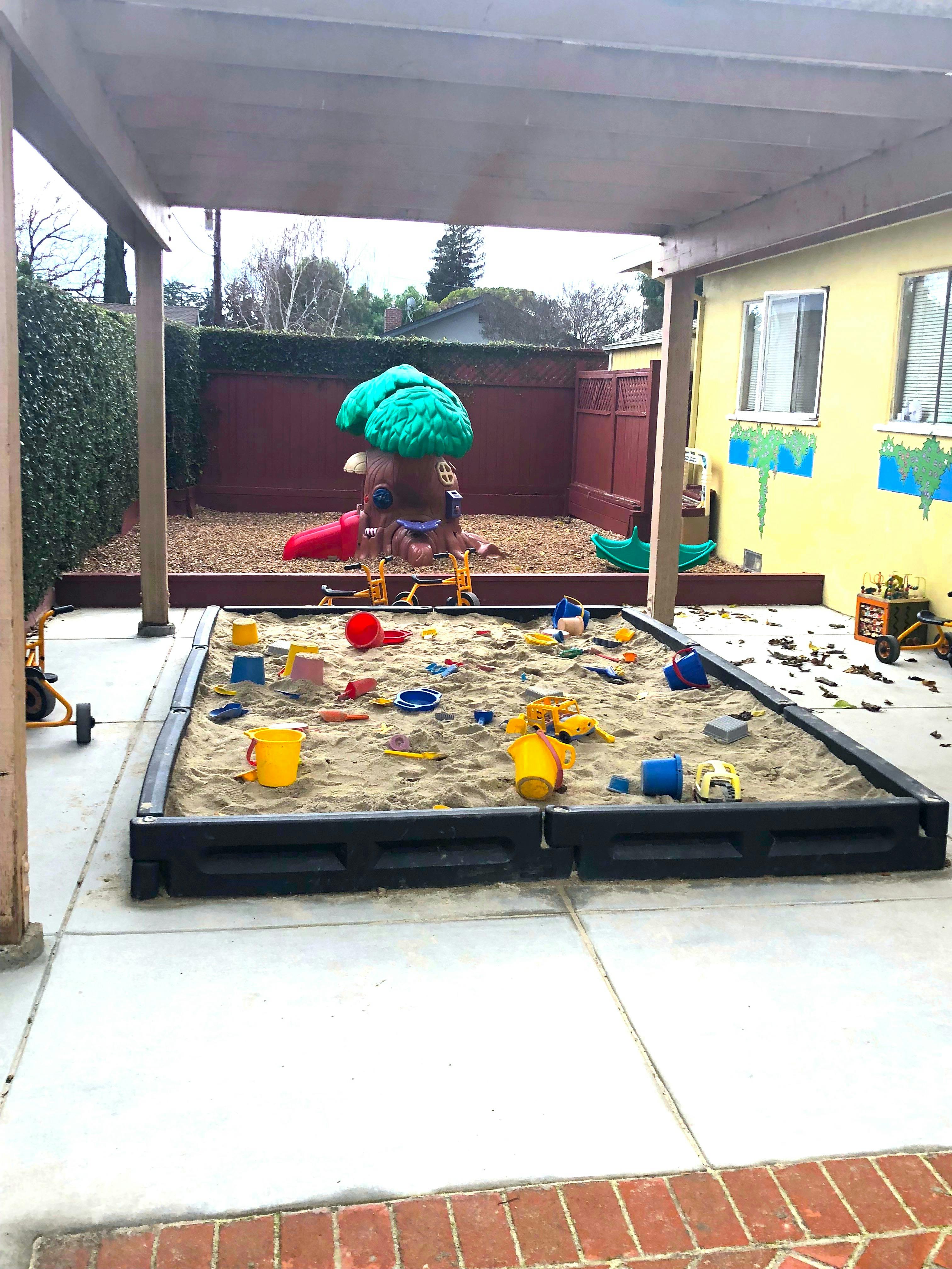 Outdoor sandbox with toys and a play structure in the background
