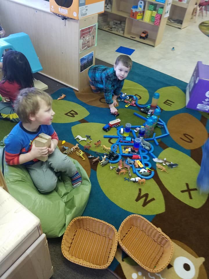 Two children playing with toys on a rug in a classroom