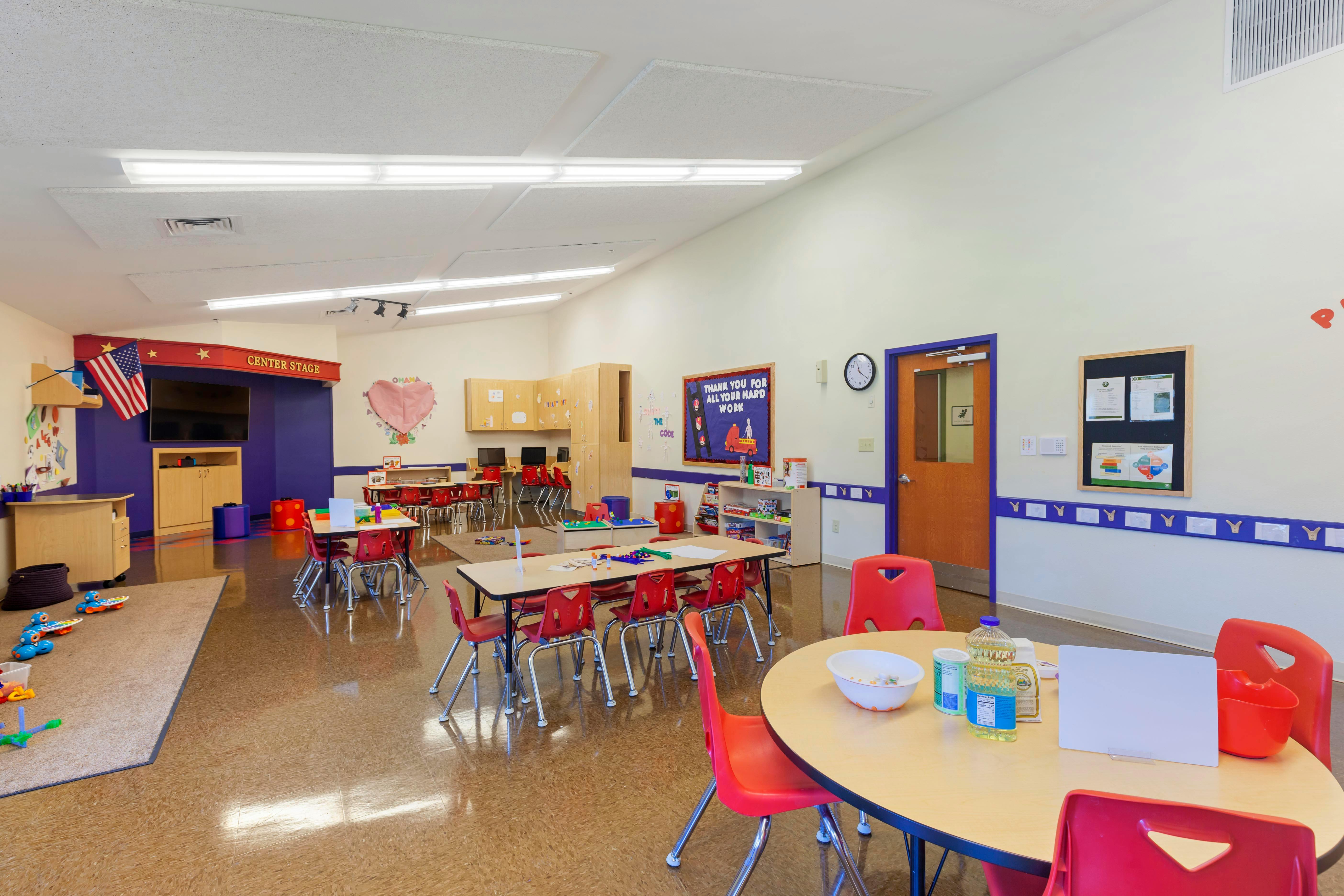 An empty classroom with small tables and red chairs