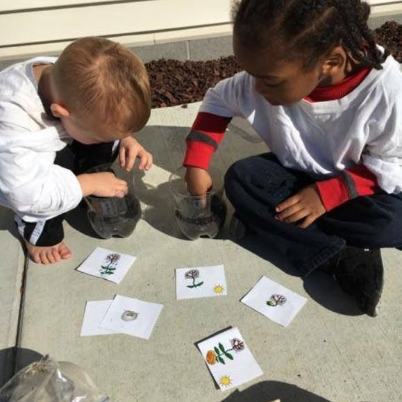 Two children playing with plastic bottles and cards with drawings on the ground